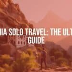 A solo traveler standing in front of the ancient Geghard Monastery in Armenia, surrounded by rocky cliffs and lush greenery, dramatic mountain backdrop, warm sunlight, realistic.